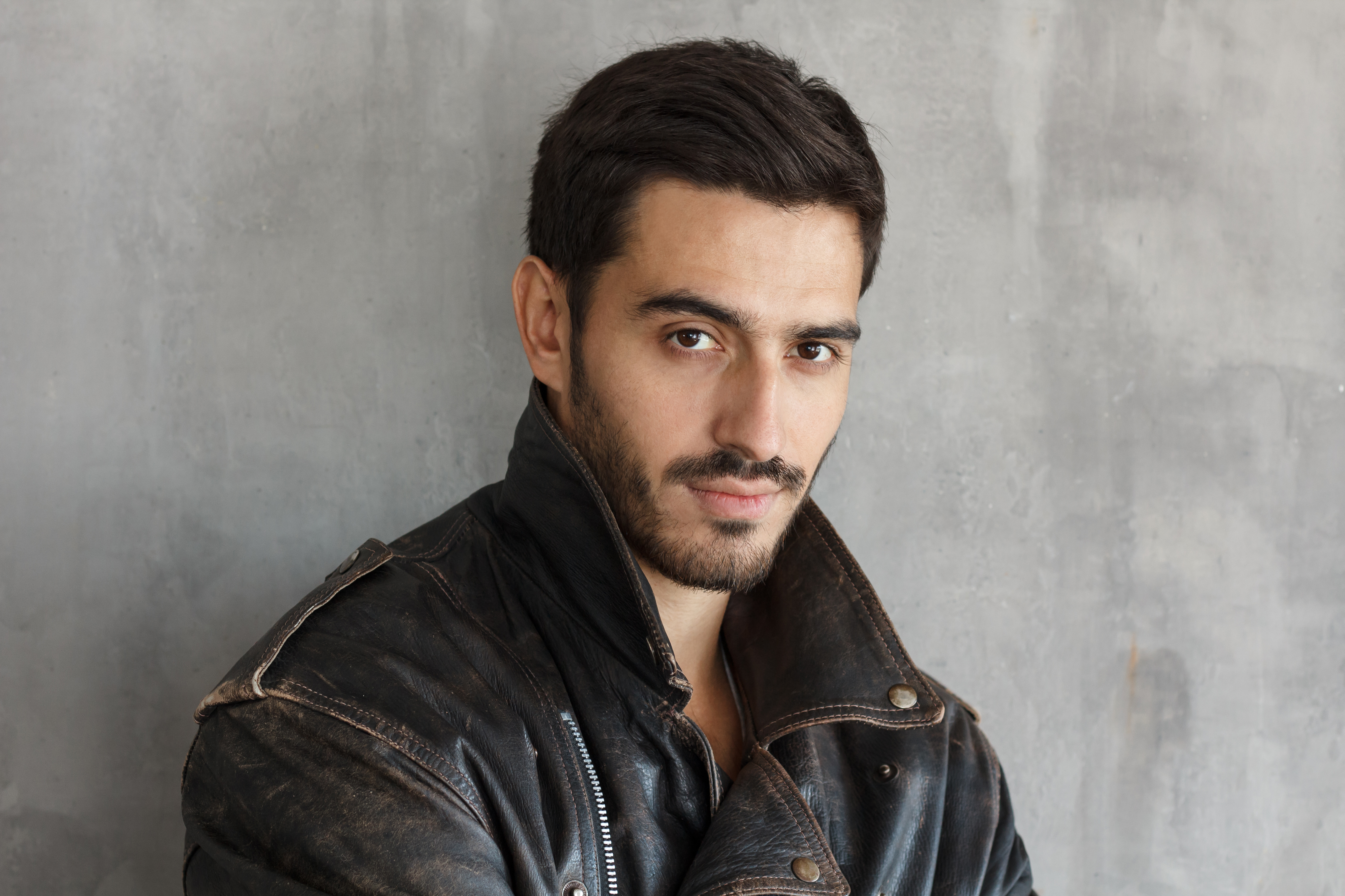 Portrait of bearded macho male dressed in brown leather jacket, looking at camera