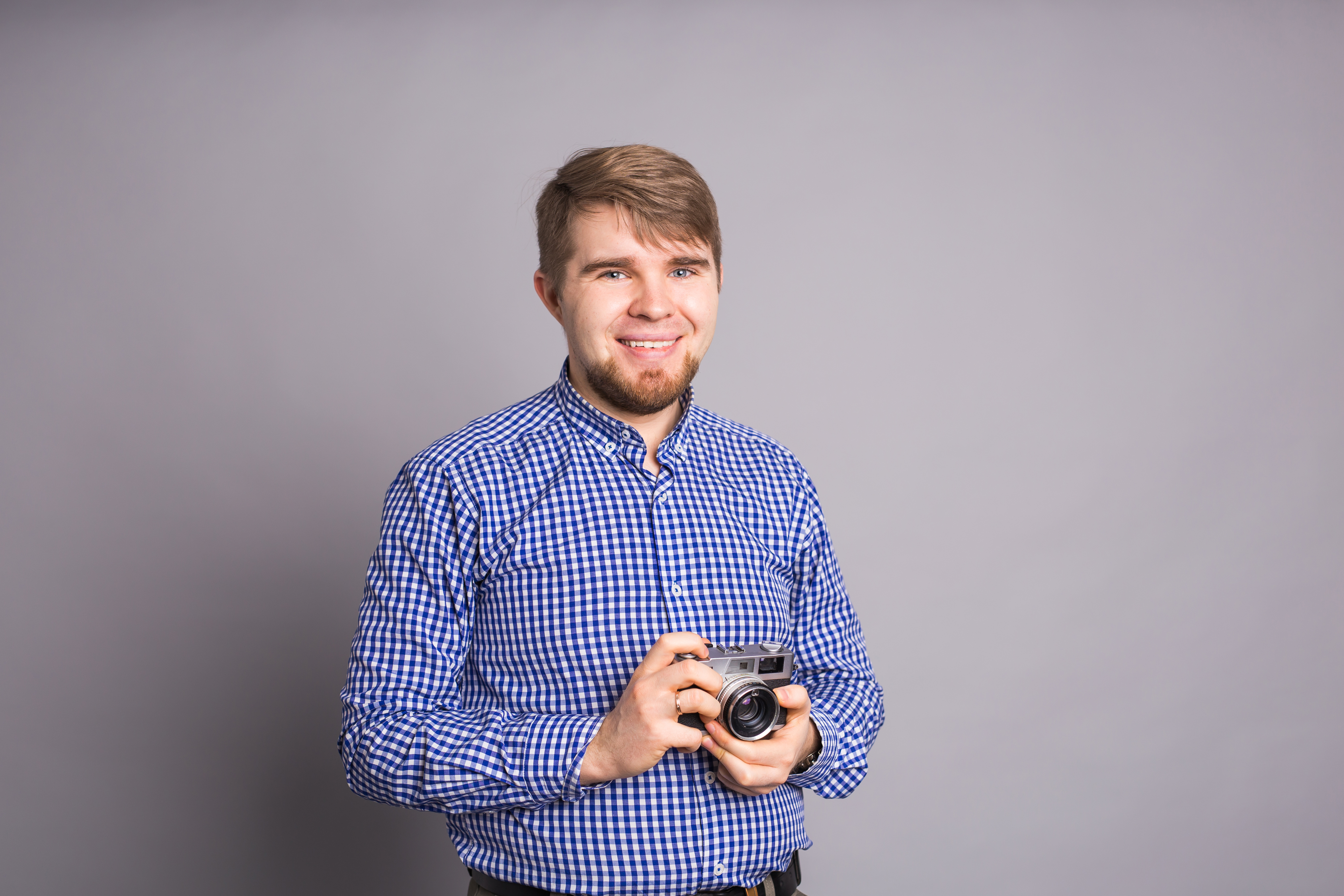 Young photographer man holding retro camera on a gray background.
